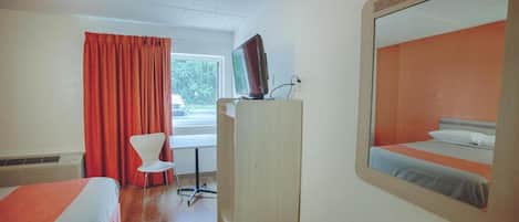 A hotel room with a bed, a desk, a chair, a television, and a window with curtains.