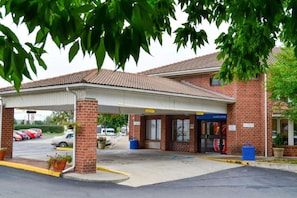 A building with a covered parking area, a brick facade, and a sign that reads 'Welcome'.