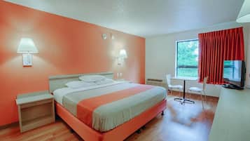 A hotel room with a bed, bedside tables, a desk, a chair, a television, and a window with curtains.