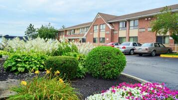 A hotel with a brick facade, a parking lot, and a landscaped garden with various plants and flowers.