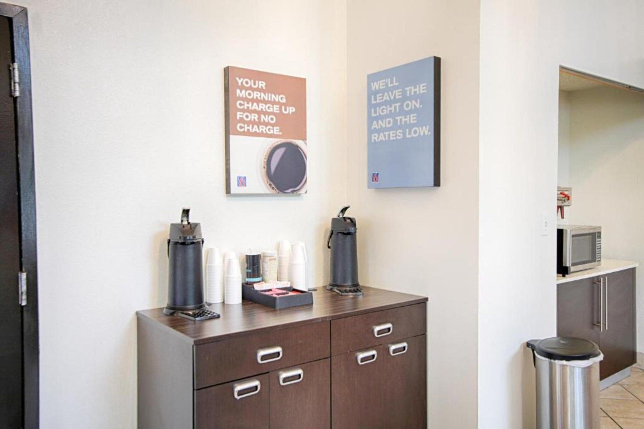 A hotel room with a minibar, a coffee machine, and two motivational posters on the wall.