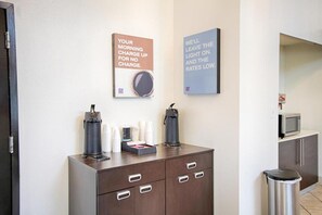 A hotel room with a minibar, a coffee machine, and two motivational posters on the wall.