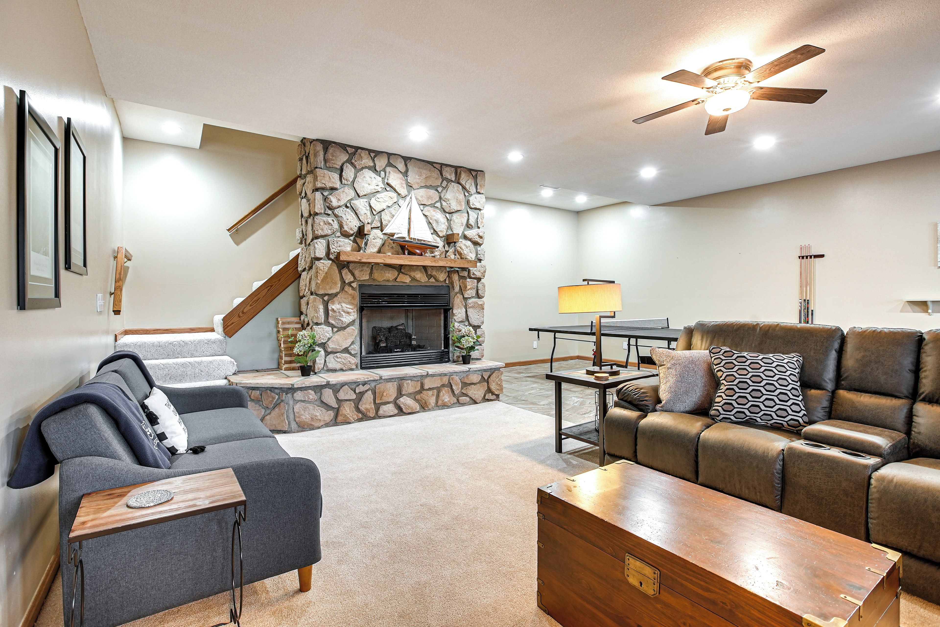 A living room with a stone fireplace, a sofa, a brown leather couch, and a wooden coffee table.