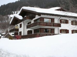 A multi-story chalet with a snow-covered roof, wooden balconies, and a mountainous backdrop. - Chlus 1 Appartement/Fewo, Dusche oder Bad, WC 2 1/2-Zimmerwohnung by Interhome (Klosters)