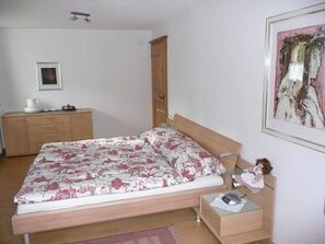 A bedroom with a bed, a nightstand, a dresser, and a framed picture on the wall. - Chlus 1 Appartement/Fewo, Dusche oder Bad, WC 2 1/2-Zimmerwohnung by Interhome (Klosters)