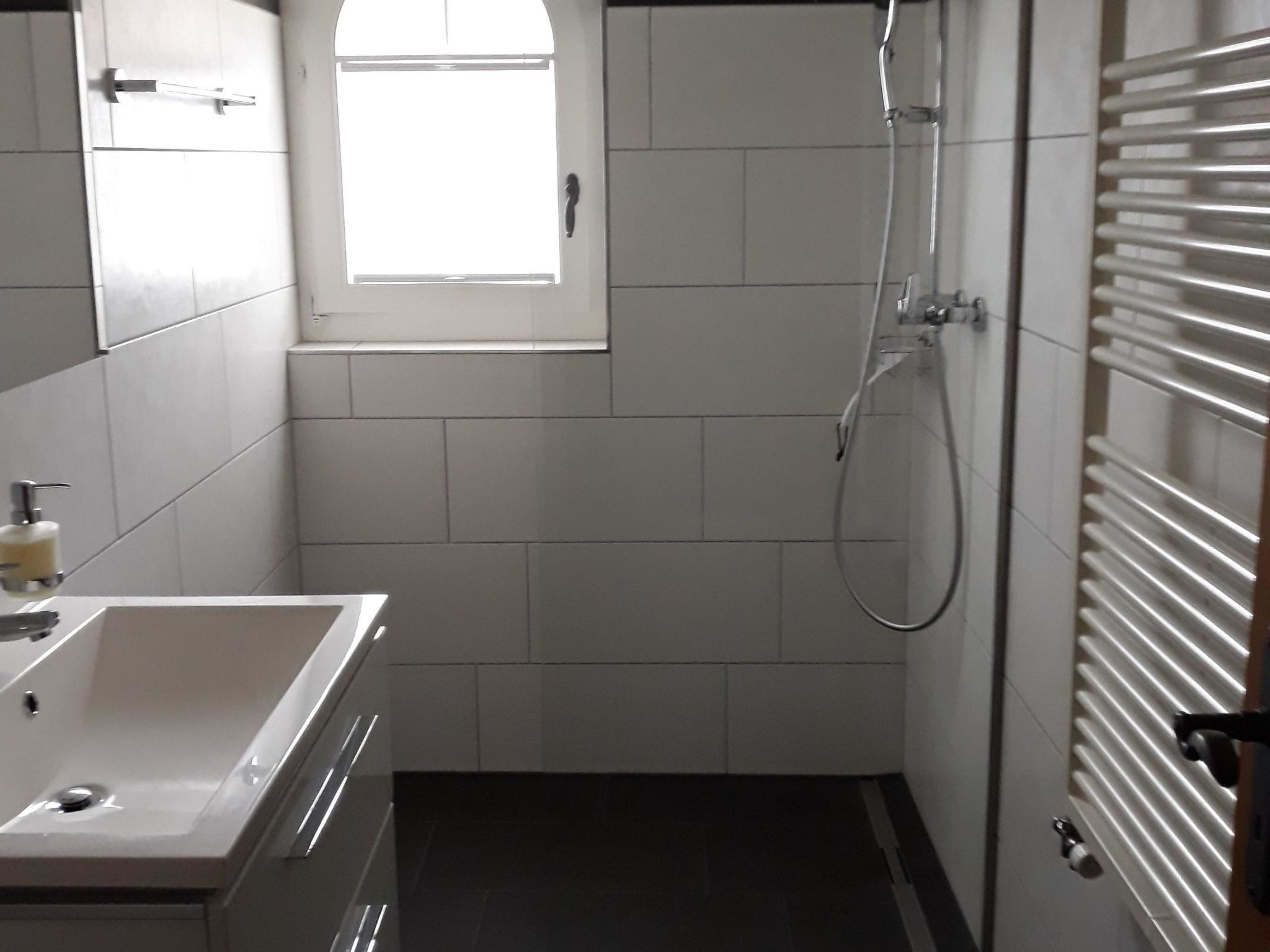 Ein Badezimmer mit einem weißen Waschbecken, einem Fenster und einer Dusche.
