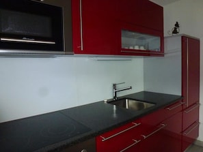 A kitchen with a black microwave, stainless steel sink, and red cabinets. - Chlus 1 Appartement/Fewo, Dusche oder Bad, WC 2 1/2-Zimmerwohnung by Interhome (Klosters)