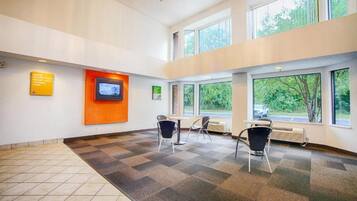 A spacious room with a checkered floor, a digital screen on the wall, and large windows offering a view of greenery outside.