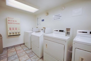 A laundry room with four washing machines, a sign listing soap, bleach, and softeners, and a notice about unattended items.