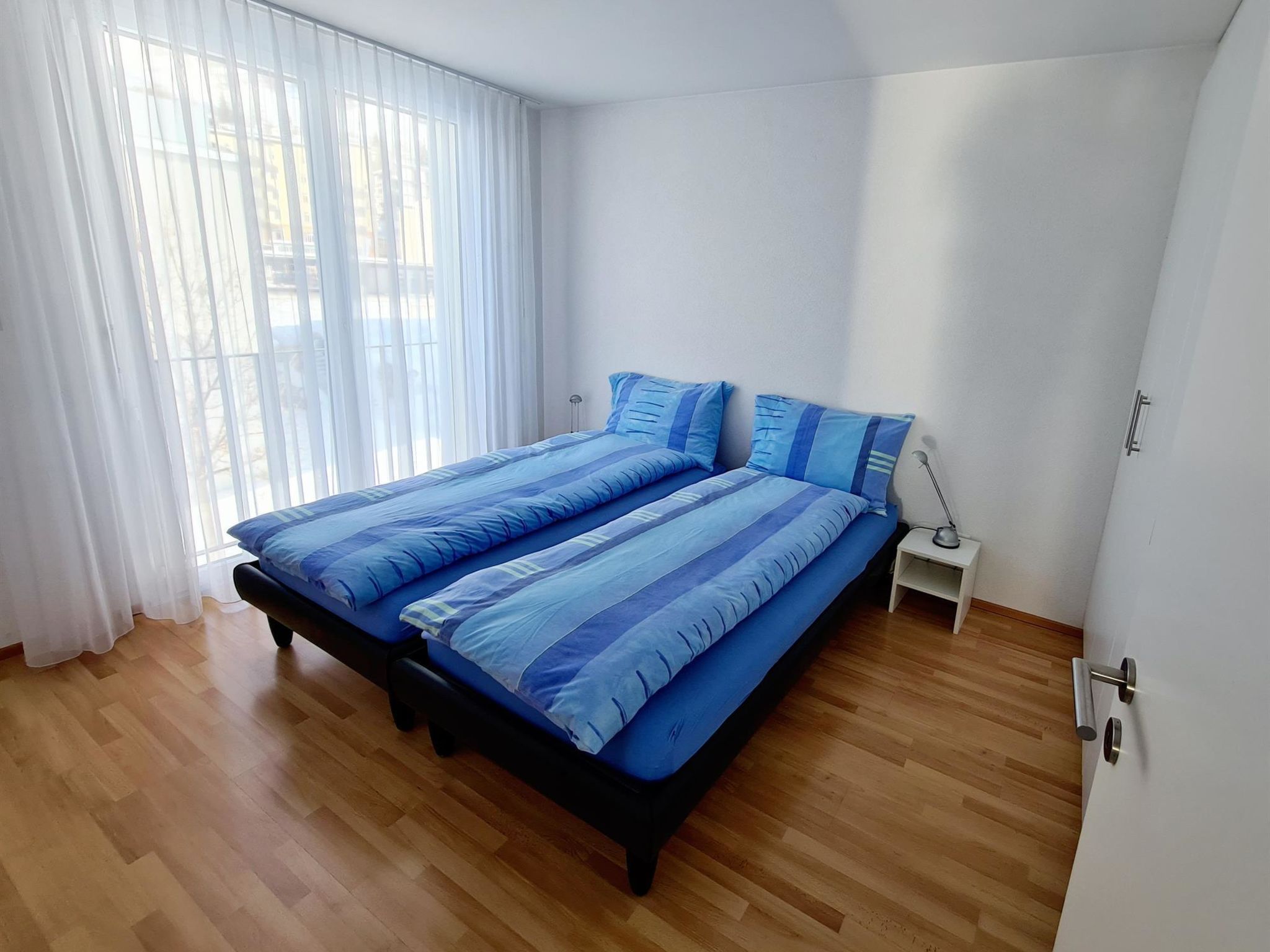 A bedroom with a bed, a nightstand, and a window with curtains.