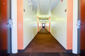 A long, narrow hallway with doors on both sides, leading to a bright room at the end.