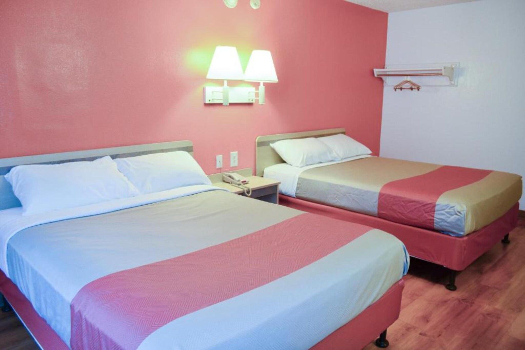 A hotel room with two beds, a bedside table with a phone, and a wall-mounted lamp.