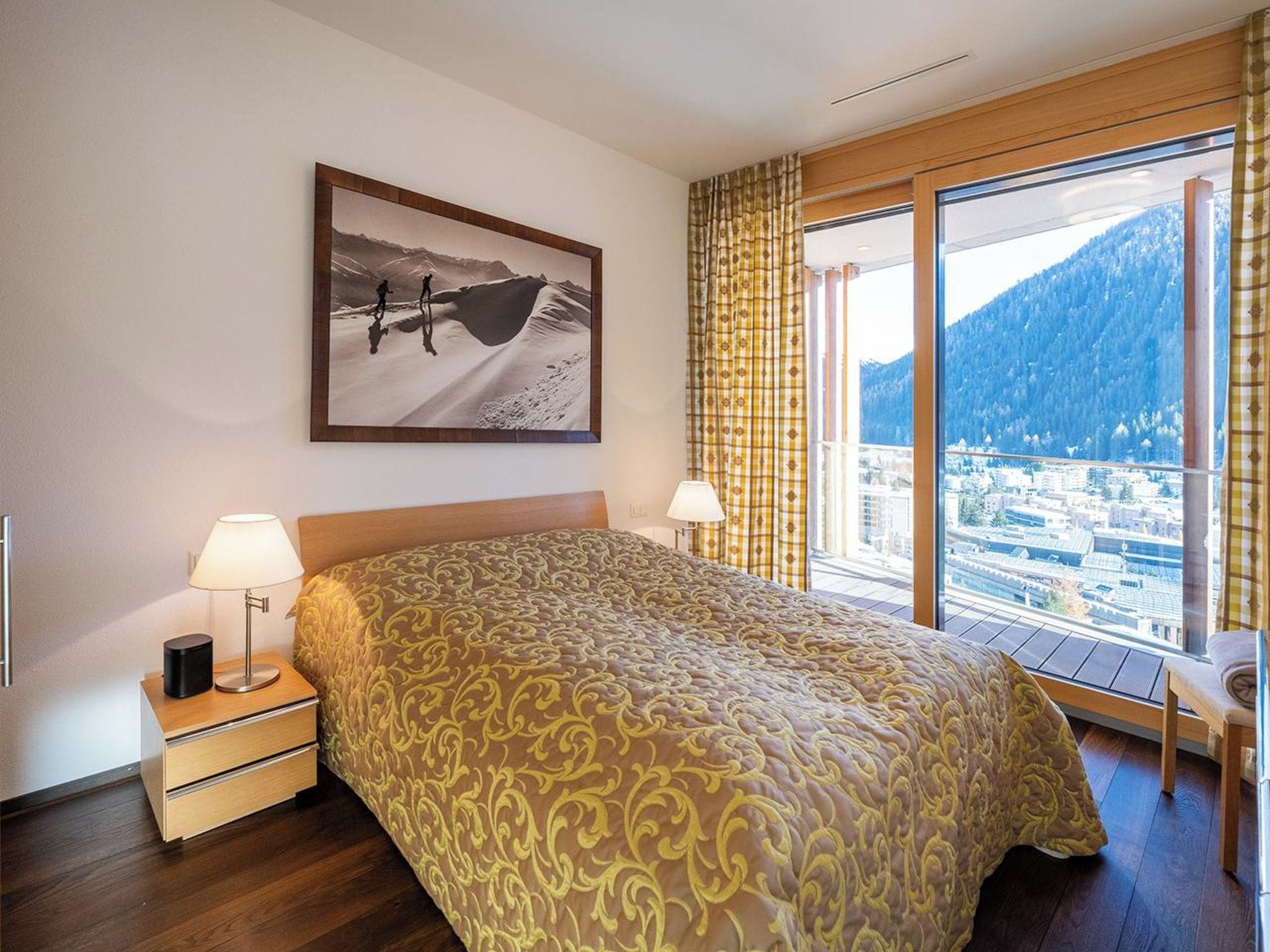 Ein Hotelzimmer mit einem großen Bett, einem Nachttisch, einer Lampe und einem Fenster mit Blick auf die Berge.
