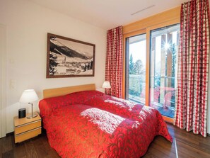 A bedroom with a large bed, a nightstand with a lamp, a window with curtains, and a framed picture on the wall. - Scarlett Suot 64 Appartement/Fewo, Dusche oder Bad, WC 4-Zimmerwohnung by Interhome (Davos)
