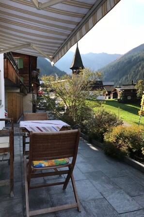 Eine Außenpatio mit Tisch und Stühlen, mit Blick auf eine gebirgige Landschaft mit einem Kirchturm.
