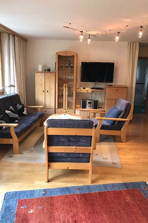 Ein Wohnzimmer mit einer Couch, zwei Holzstühlen, einem Fernseher und einem Schrank.