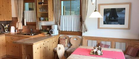 Una cocina acogedora con armarios de madera, una mesa de comedor con sillas y un ventanal con cortinas.