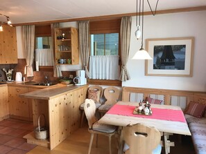 Eine gemütliche Küche mit Holdekor-Schränken, einem Esstisch mit Stühlen und einem Fenster mit Vorhängen.