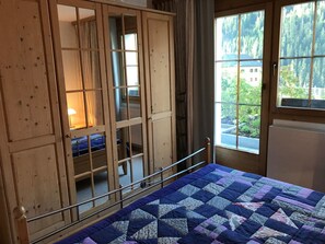 Een kamer met een stapelbed, een houten garderobe en een raam met uitzicht op een bos.