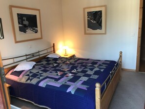 Ein Schlafzimmer mit einem Bett, zwei gerahmten Bildern an der Wand, einer Nachttischlampe und einem hölzernen Kopfteil.