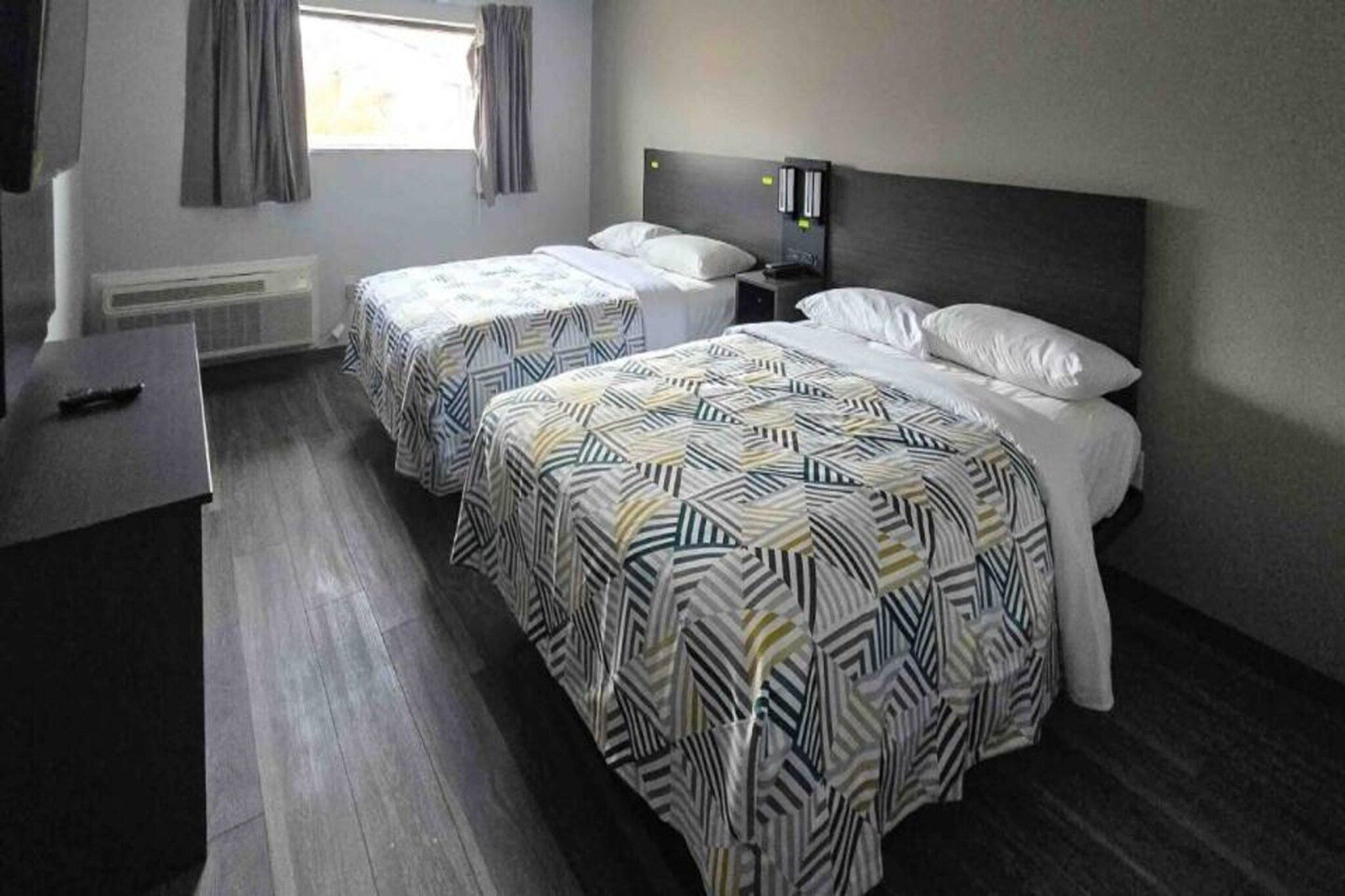 Une chambre d’hôtel avec deux lits, un bureau et une fenêtre avec des rideaux.