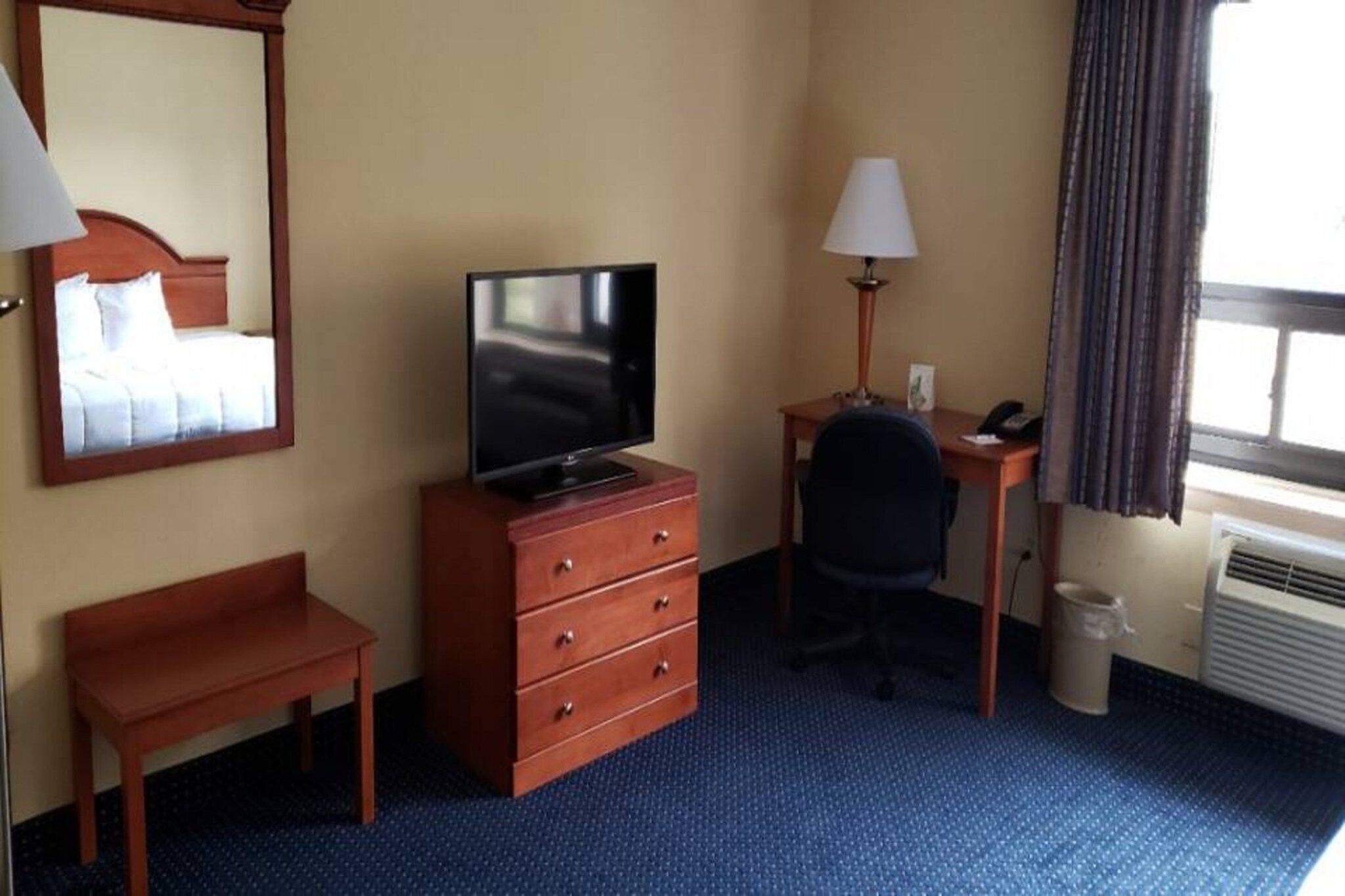 Hotellihuone, jossa on sänky, työpöytä tuolilla, televisio, lamppu ja roskakori.