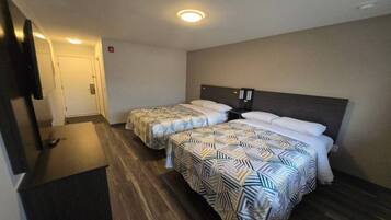 A hotel room with two beds, a television, and a wooden floor.