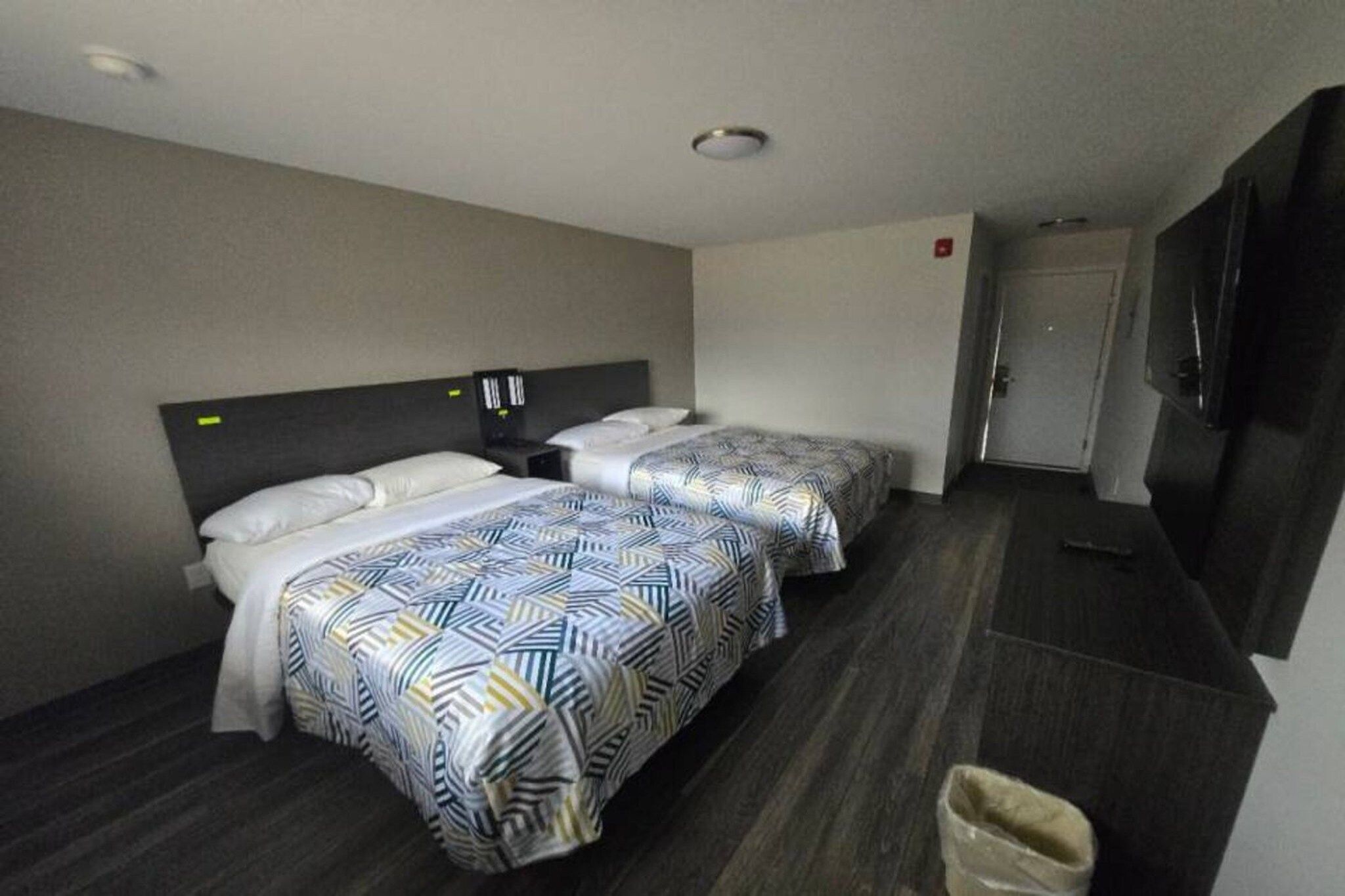 A hotel room with two beds, a television, and a trash bin.