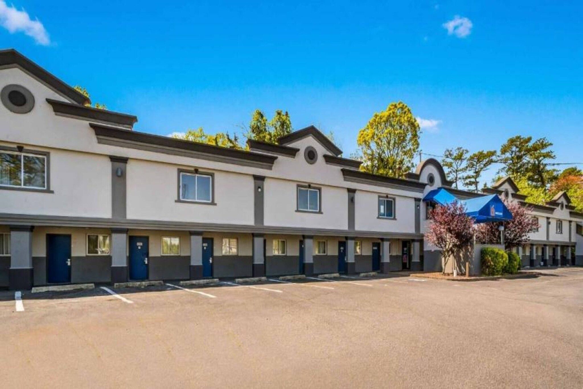 A hotel with a row of rooms, a parking lot, and a blue awning.
