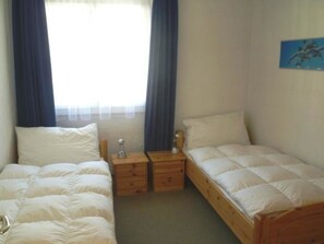 Een slaapkamer met twee bedden, een nachtkastje en een raam met gordijnen.