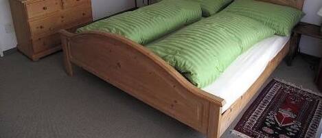 A bedroom with a wooden bed, a dresser, a nightstand, a lamp, and a wall-mounted mirror.