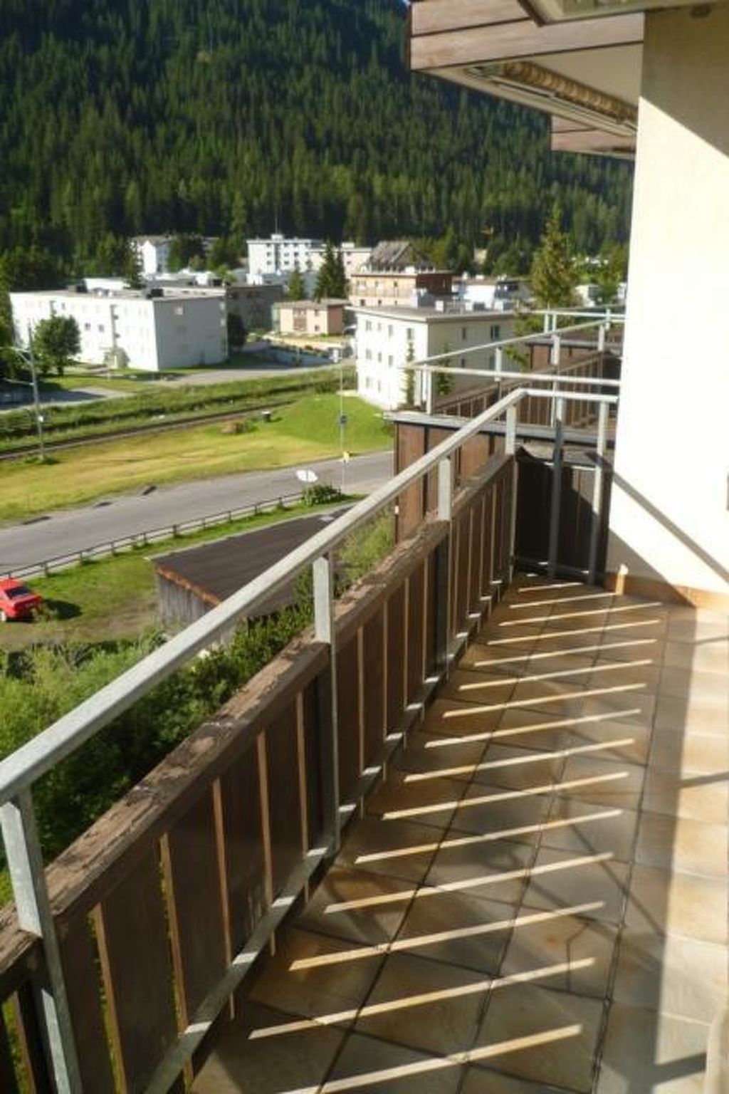 A balcony with a view of a road and buildings, a tiled floor, and a metal railing.