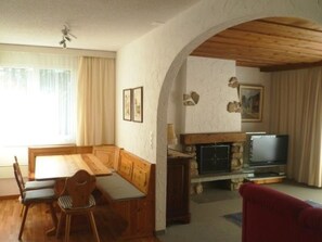 A living room with a wooden dining table, chairs, a sofa, a fireplace, and a television. - Golfresidenz 47 Appartement/Fewo, Dusche oder Bad, WC 4½-Zimmerwohnung by Interhome (Davos)
