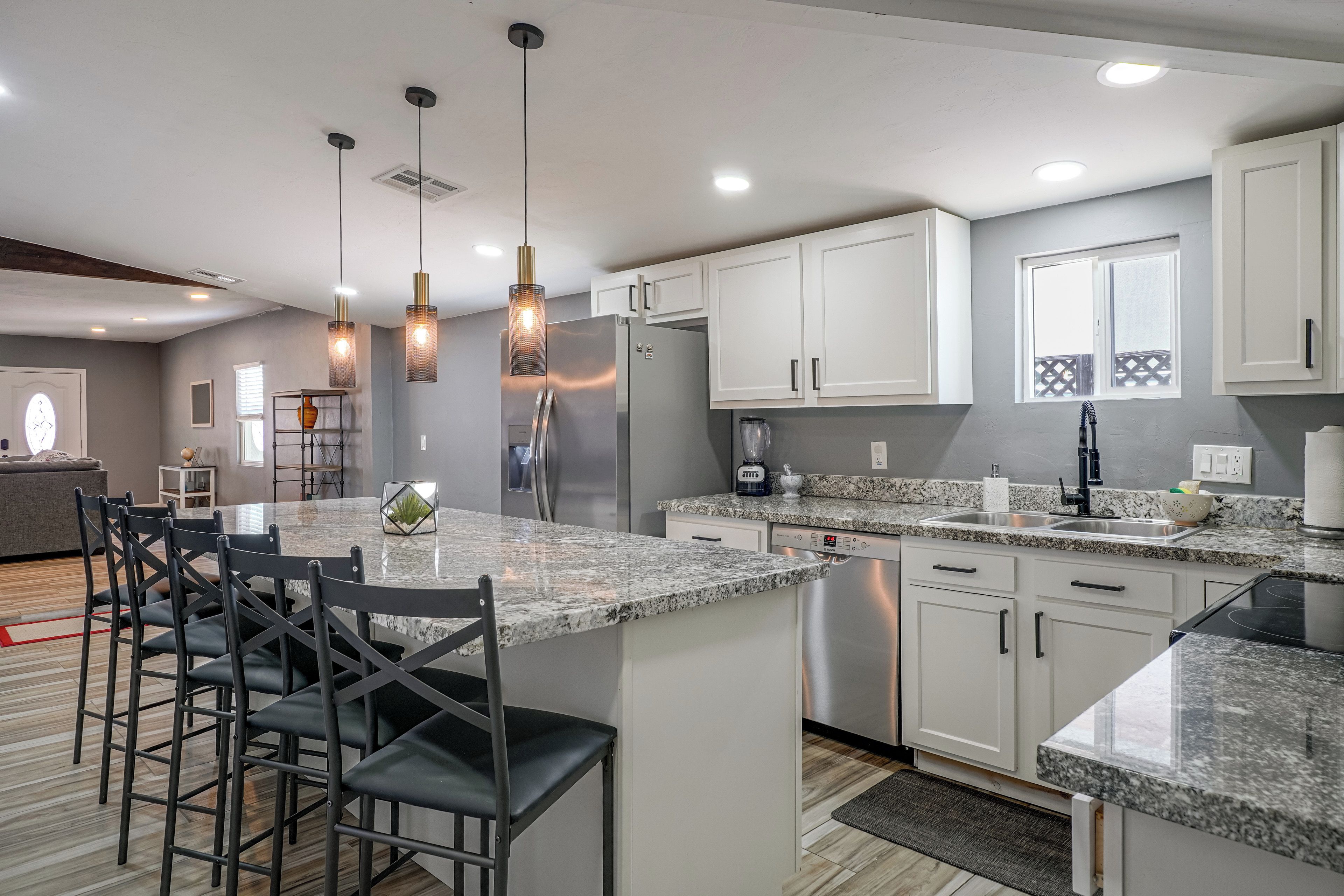 A modern kitchen with a central island, bar stools, stainless steel appliances, and pendant lighting.