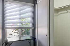 Ein Zimmer mit Fenster, das mit Jalousien verdeckt ist, einem kleinen Tisch und einer Tür.