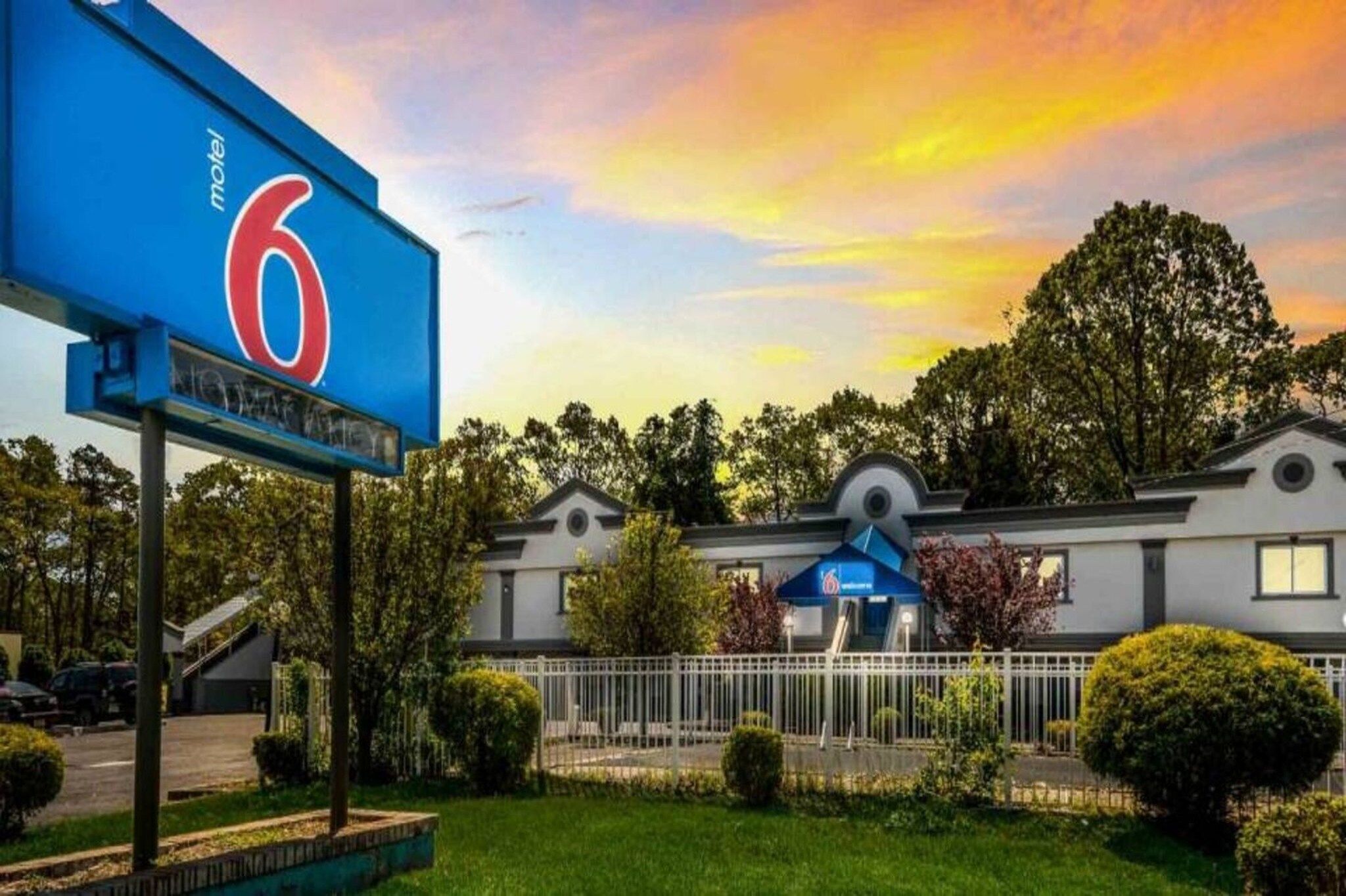 A motel with a prominent '6' sign, a covered outdoor seating area, and a well-maintained lawn.
