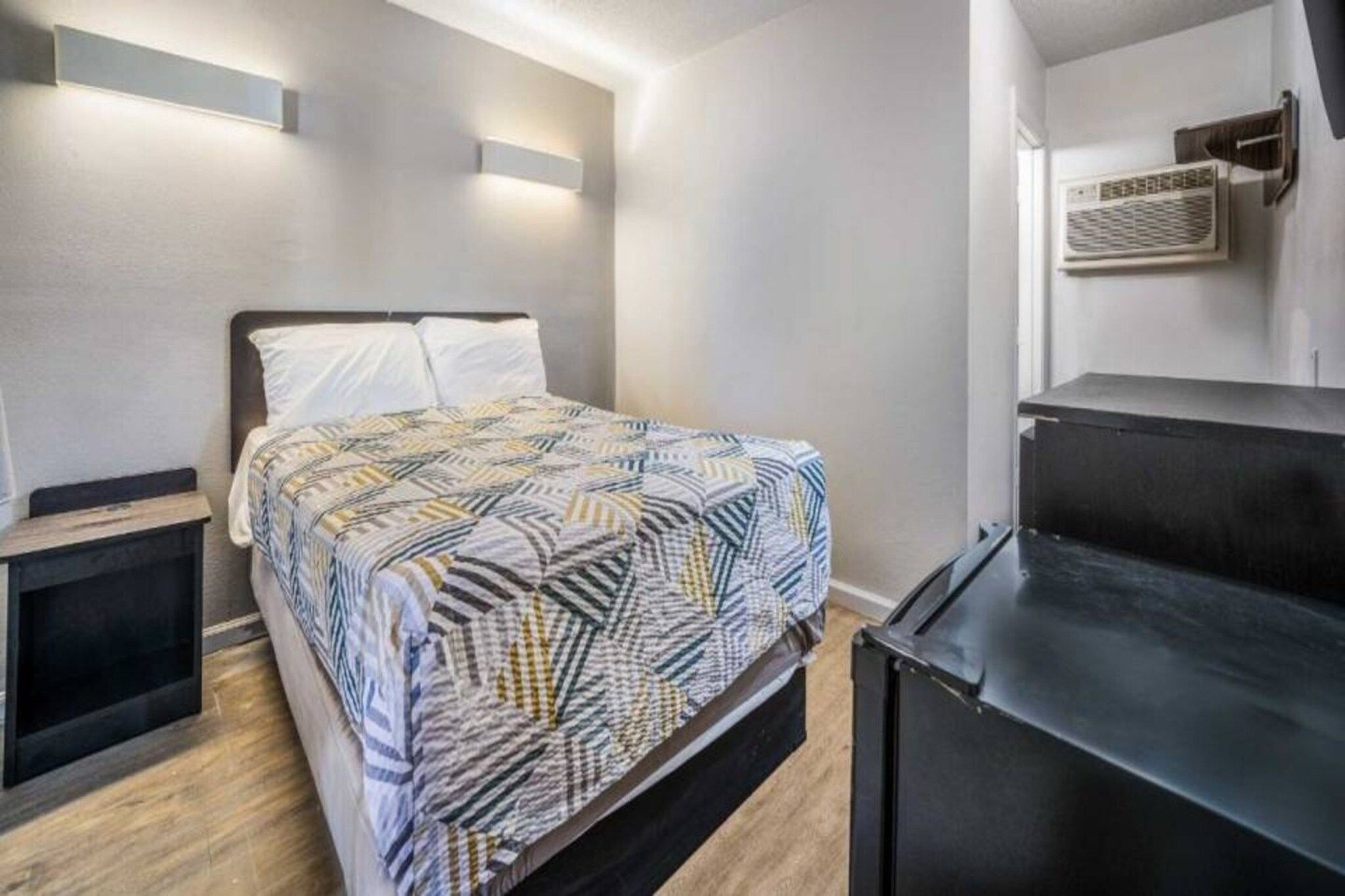 A bedroom with a bed, bedside tables, a black dresser, and a wall-mounted air conditioning unit.