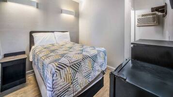 A bedroom with a bed, bedside tables, a black dresser, and a wall-mounted air conditioning unit.