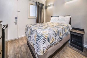 A bedroom with a bed, a bedside table, a window with curtains, and a door.