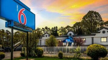 A motel with a prominent '6' sign, a covered outdoor seating area, and a well-maintained lawn.