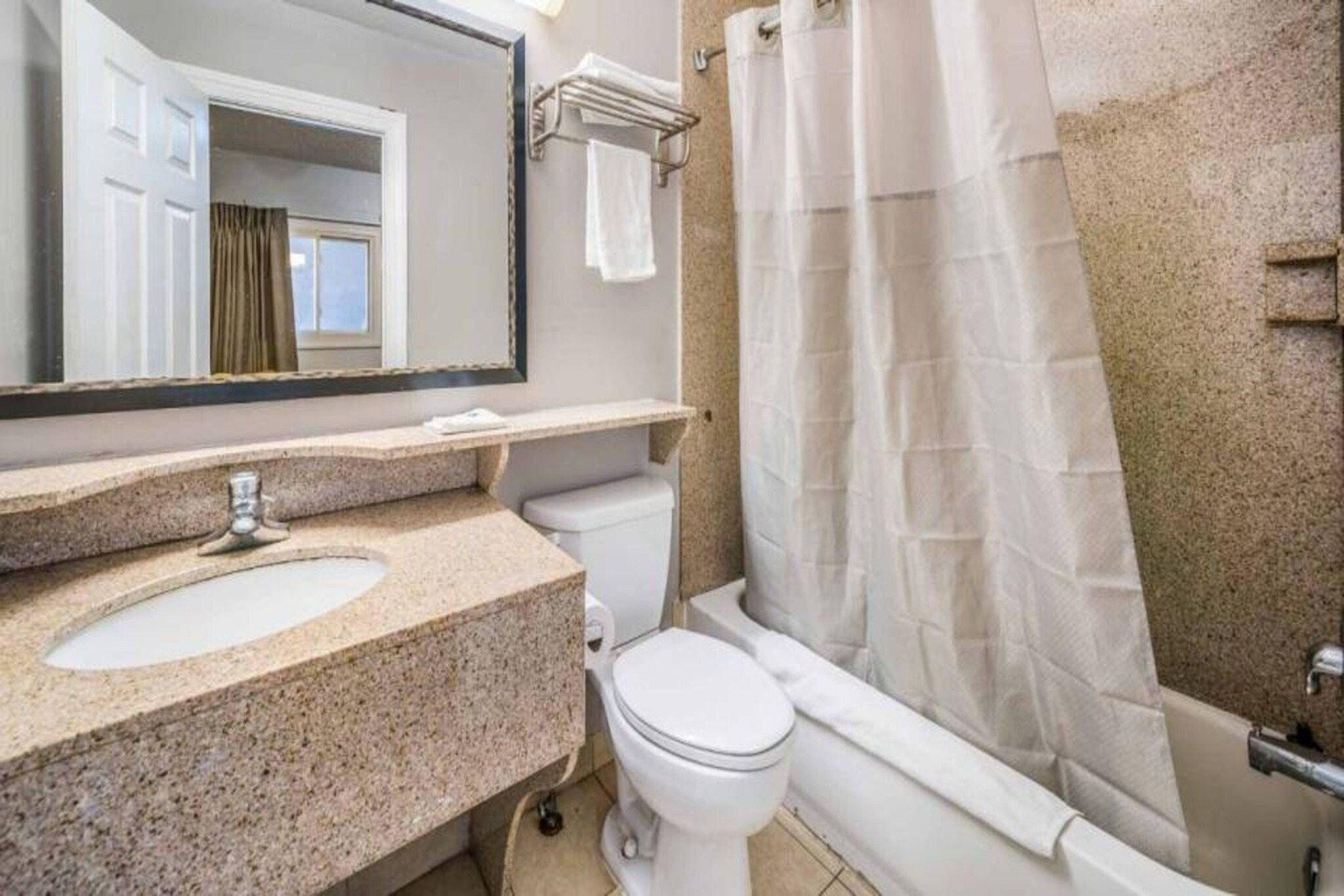 A bathroom with a granite countertop sink, a white toilet, a bathtub with a shower curtain, and a mirror above the sink.