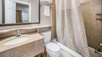 A bathroom with a granite countertop sink, a white toilet, a bathtub with a shower curtain, and a mirror above the sink.