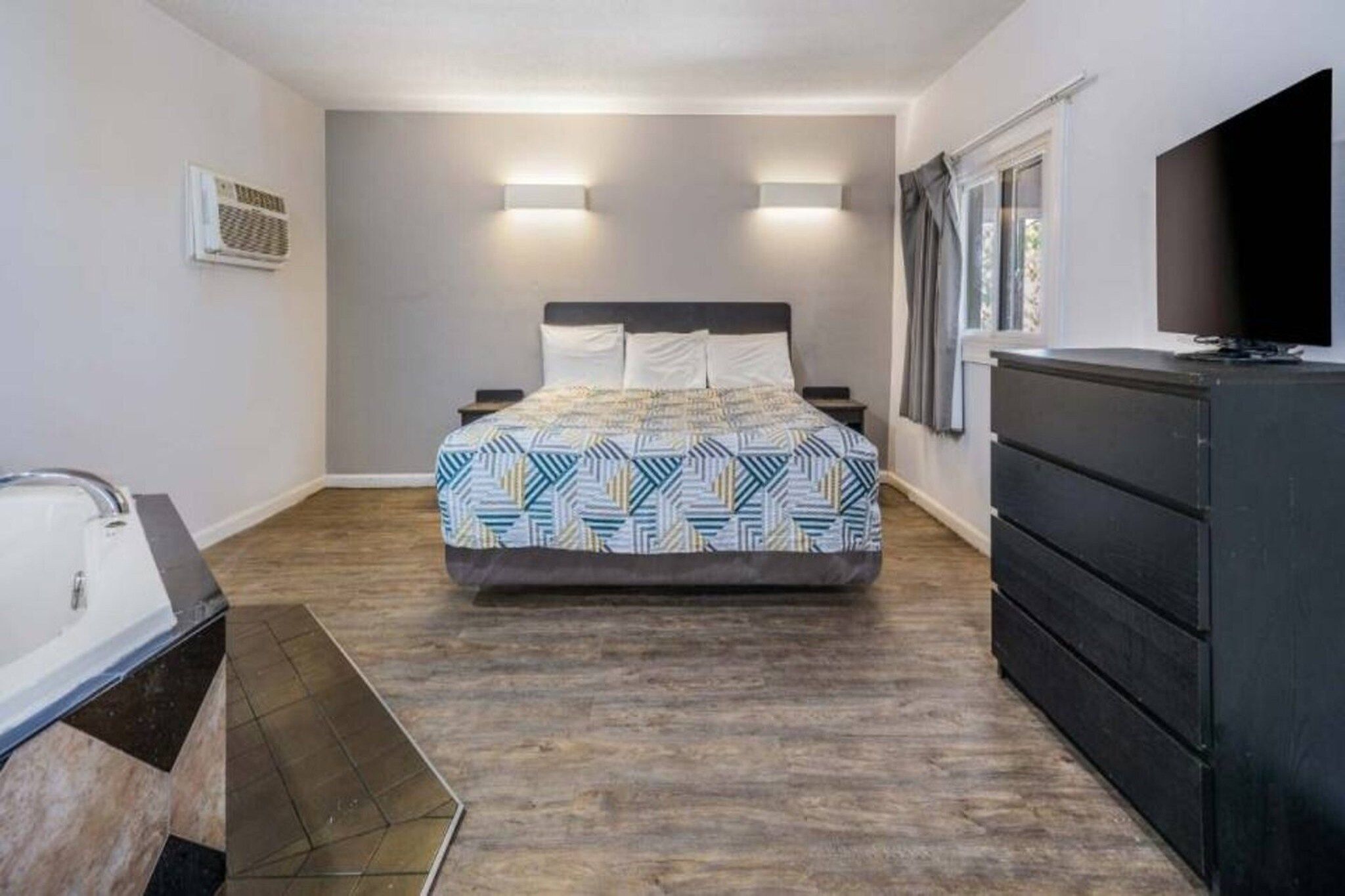 A bedroom with a bed, a dresser, a TV, and a window.
