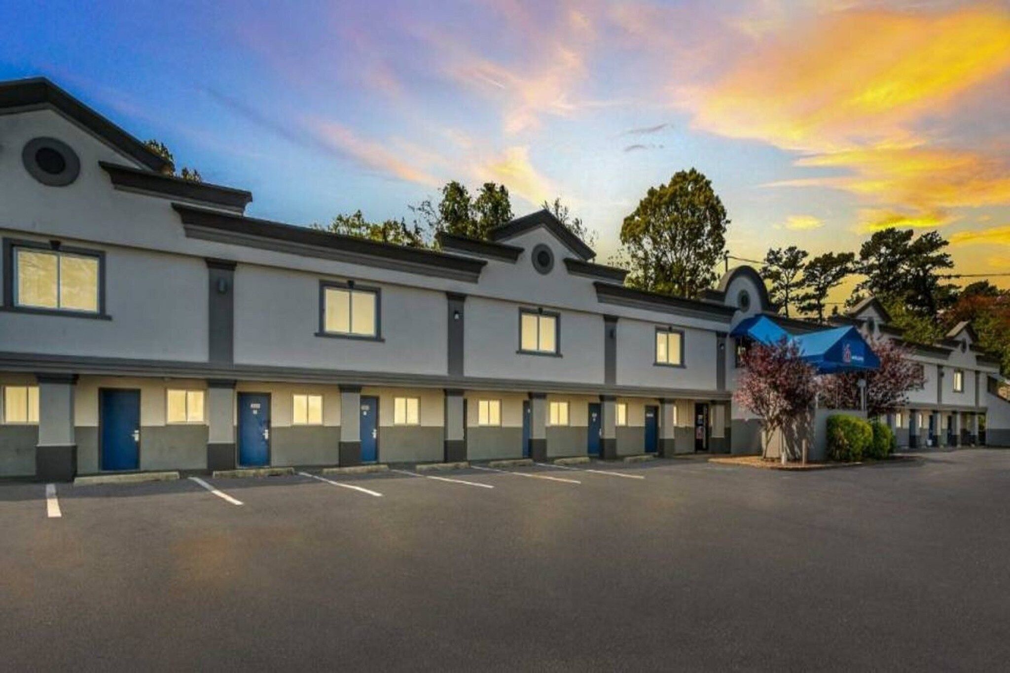 A row of motel rooms with a parking lot in front.