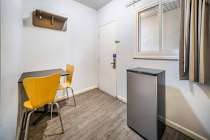 Ein kleiner Raum mit Tisch, zwei Stühlen, einem Kühlschrank, einer Tür und einem Fenster.