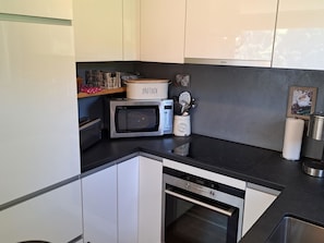 Eine kompakte Küche mit weißen Schränken, einer Mikrowelle, einem Toaster und einem Wasserkocher.
