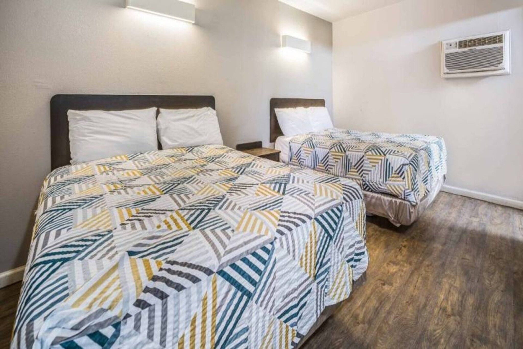 Une chambre d’hôtel avec deux lits, chacun agrémenté de draps à motifs, un plancher en bois et un appareil de climatisation fixé au mur.