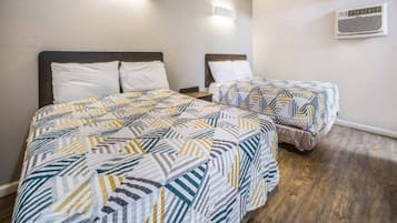 Ett hotellrum med två sängar, var och en med mönstrat sänglinne, ett trägolv och en luftkonditioneringsenhet på väggen.