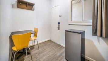 Ein kleiner Raum mit Tisch, zwei Stühlen, einem Kühlschrank, einer Tür und einem Fenster.