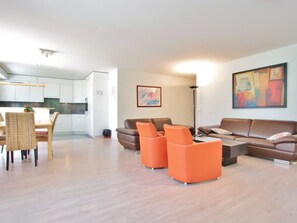 A modern living room with a brown sofa set, orange armchairs, and a dining area with a wicker table and chairs. - Auf der Matta E01 Appartement/Fewo, Dusche oder Bad, WC 4½-Zimmerwohnung by Interhome (Davos)
